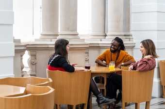 Three people sitting at a table together with drinks talking and smiling