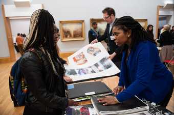 An adult giving a student advice on their art portfolio in a gallery