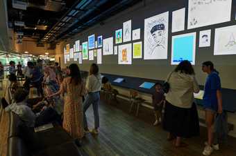 Lots of people at a digital drawing bar that displays digital drawings on the wall